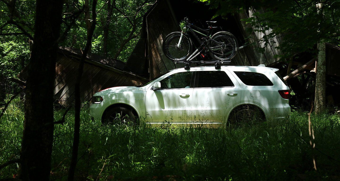 A White 2020 Dodge Durango with a bike rack and bike on the roof in a forest.