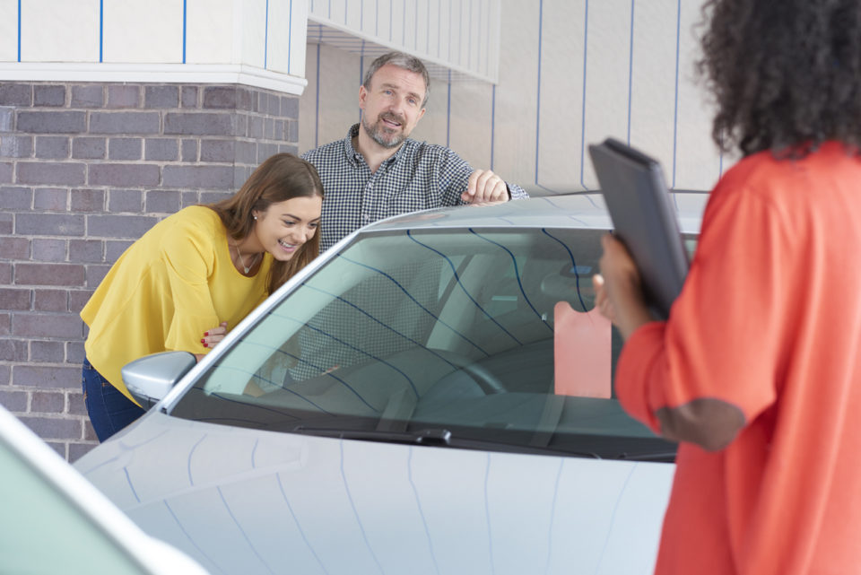 A father and daughter explore a used car while a salesperson answers their questions