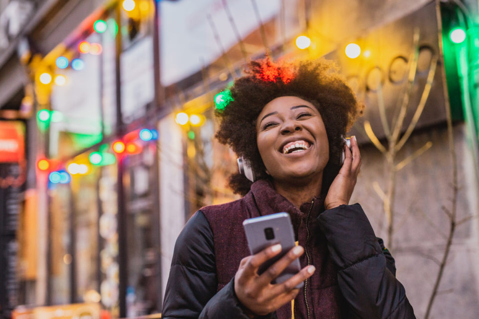 A young woman is using a mobile phone and wireless headphones outdoor during Christmas