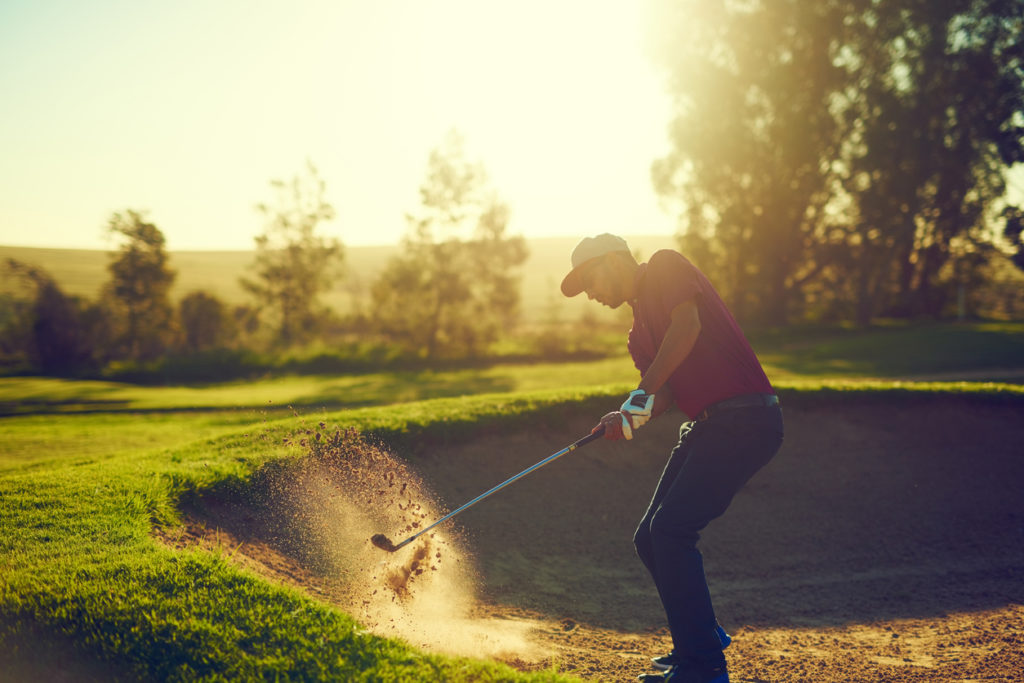 man hitting the ball out of the bunker with sun glare in background