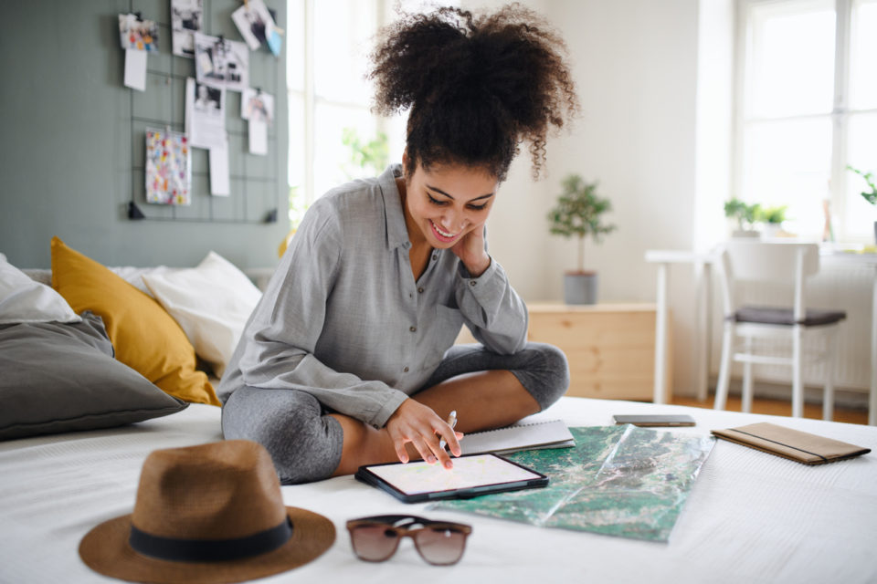 Young woman with tablet and map indoors at home, planning traveling trip.