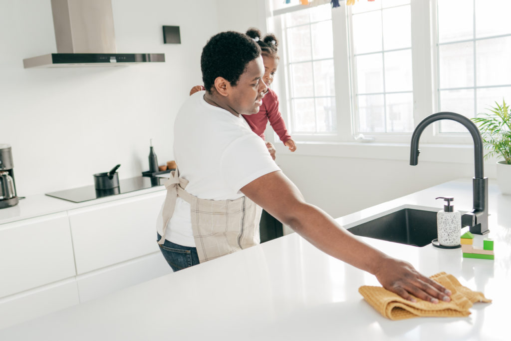 Dad and toddler daughter at home wiping off kitchen counters