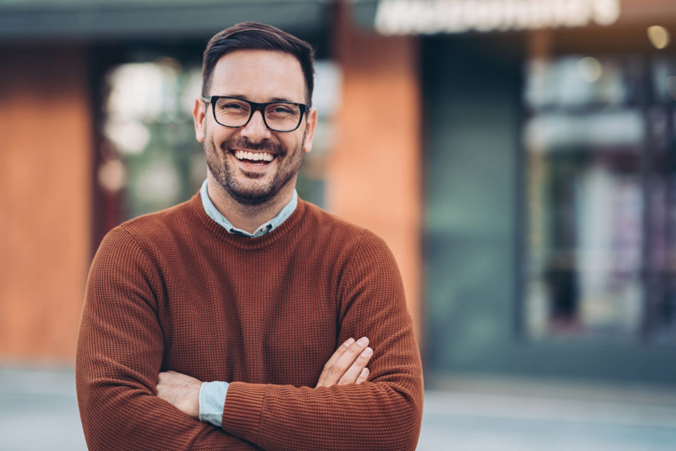 Smiling man outdoors in the city wearing orange sweater.